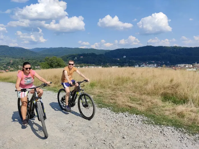 A couple riding e-bikes across a hillside meadow above the town of Sovata